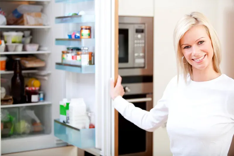 Woman at home looking inside the fridge and smiling